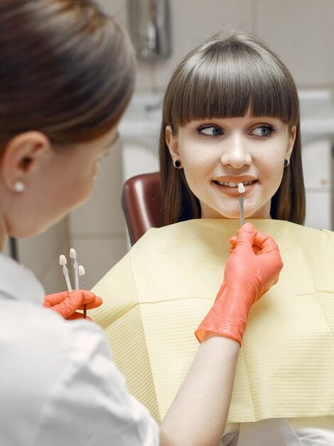 Dentist consults a young woman on veneers using dental tools and mirror in a clinic.